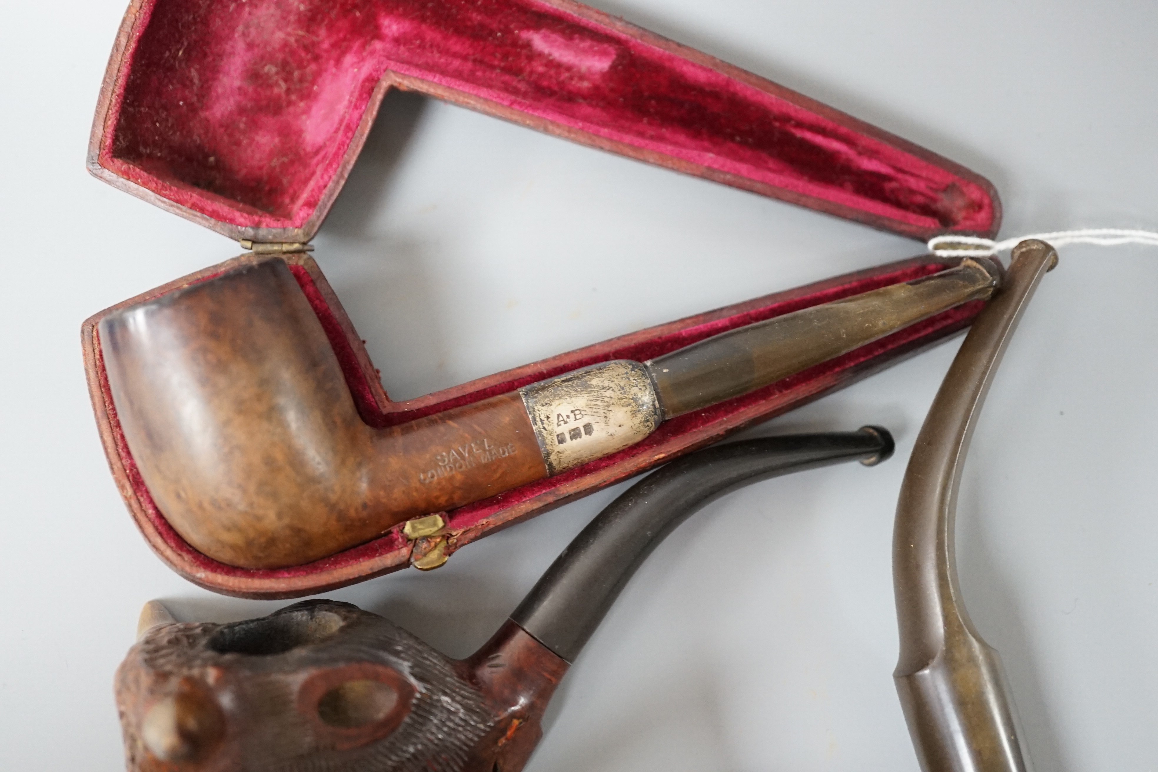 A cased Savel burr wood smokers pipe with silver collar, another pipe with silver collar and rim together with a novelty carved wood and horn ‘cow’ pipe